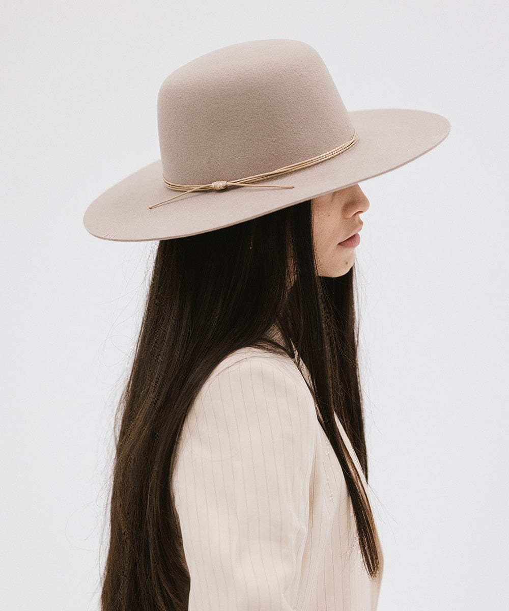 Woman wearing a sand colored open crown hat with a hat band and a cream blazer, facing sideways against a plain background #color_sand