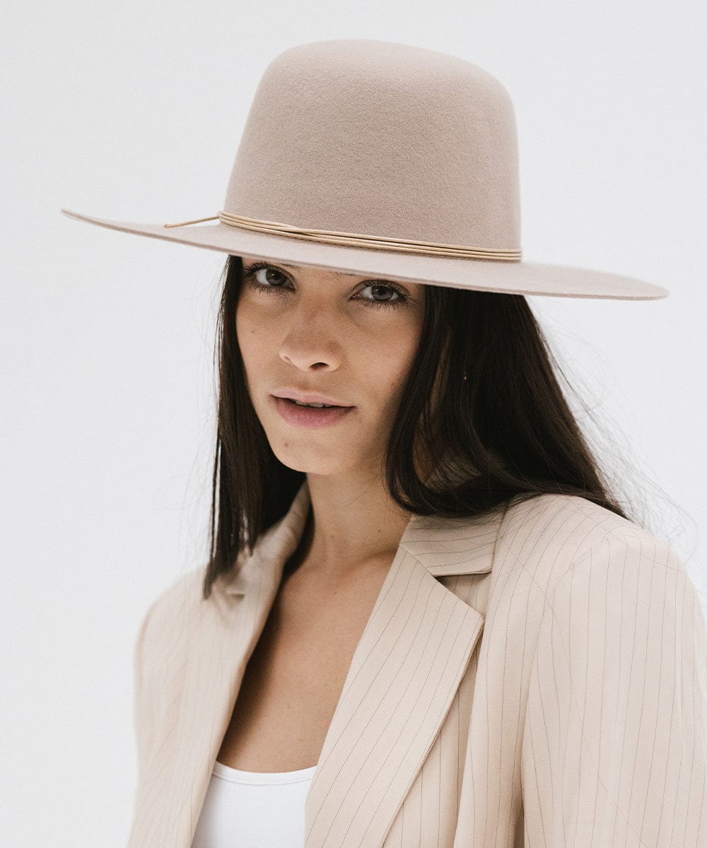 Woman wearing a sand colored open crown hat with a hat band and a cream blazer against a plain background #color_sand