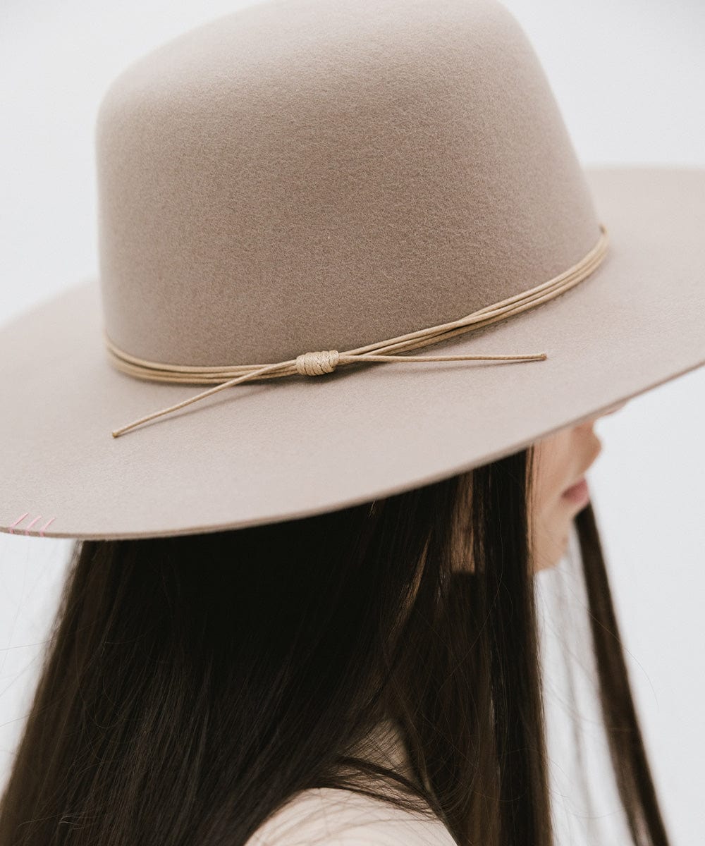 Woman wearing a sand colored open crown hat with a hat band, facing sideways against a plain background #color_sand #color_sand