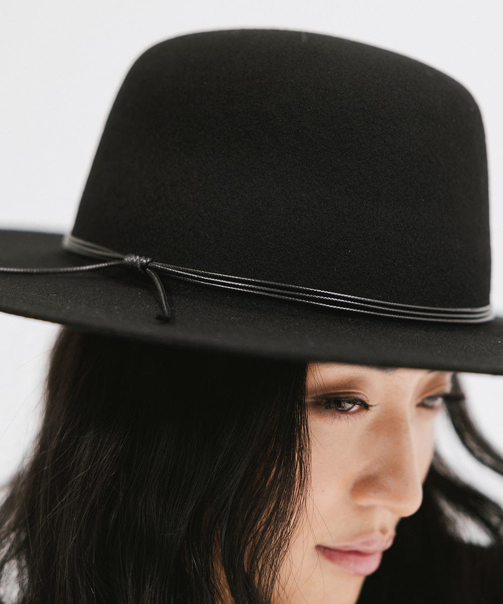 Woman wearing a black open crown hat with a hat band against a plain background #color_black