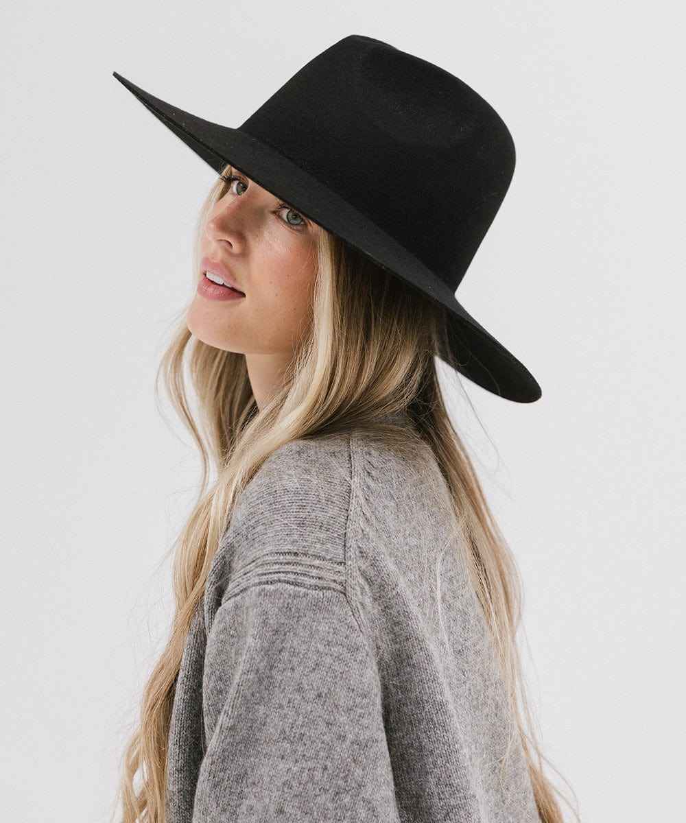 Woman wearing a black wide brim fedora hat and a grey sweater, posing against a plain background #color_black