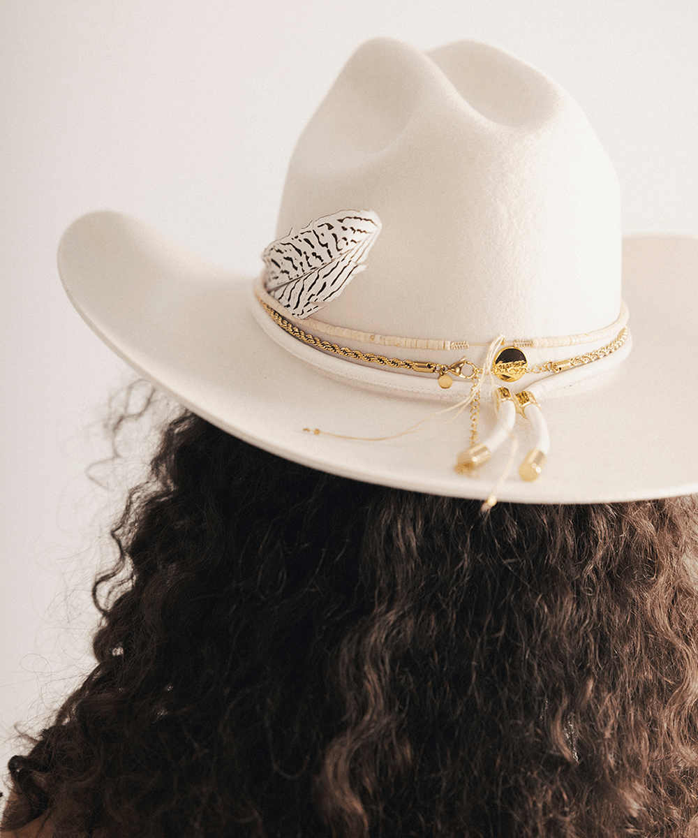 Woman wearing a white cowboy hat with a decorative band and feather on a plain background #color_off white