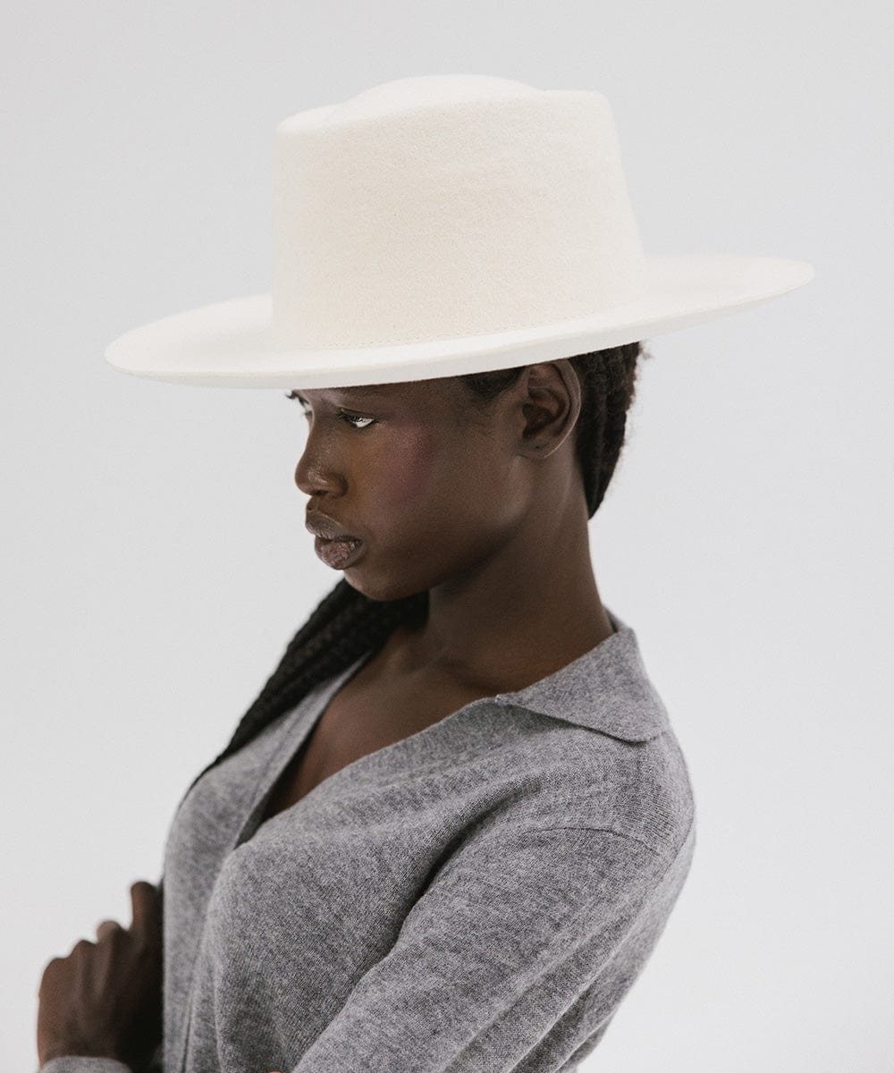Woman wearing an off white gambler hat and a grey shirt, facing sideways  against a plain background #color_off white