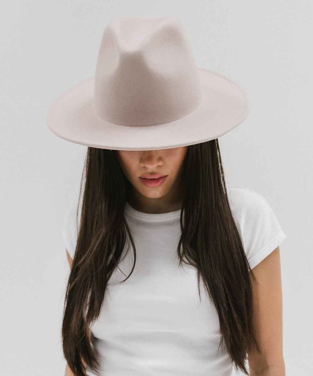 Person wearing an ivory colored fedora hat and white t-shirt on a plain background #color_ivory