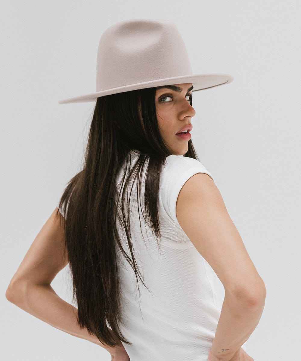 Woman wearing an ivory colored fedora hat and a white t-shirt against a plain background #color_ivory
