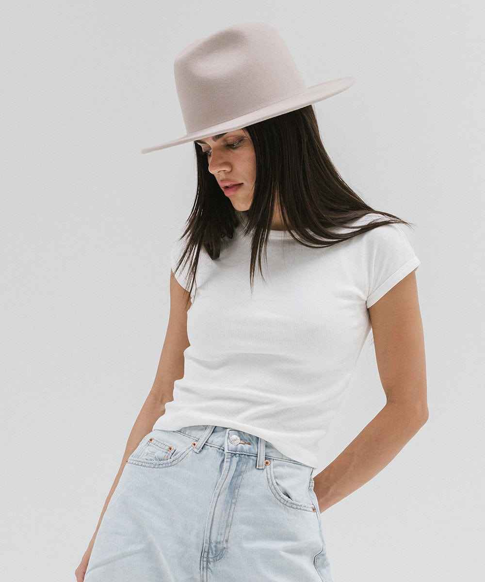 Woman wearing an ivory colored fedora hat, a white t-shirt, and light blue jeans against a plain background #color_ivory