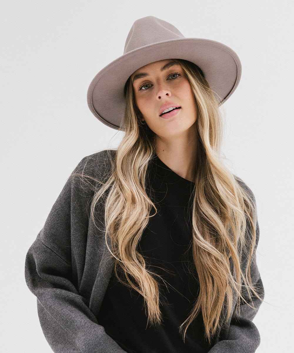 Woman wearing a light grey fedora hat and a dark grey jacket with a black top against a plain background #color_light grey