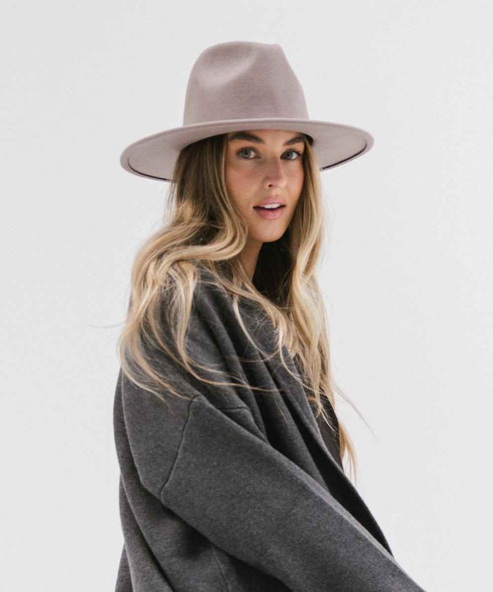 Woman wearing a light grey fedora hat and a dark grey jacket against a plain background #color_light grey