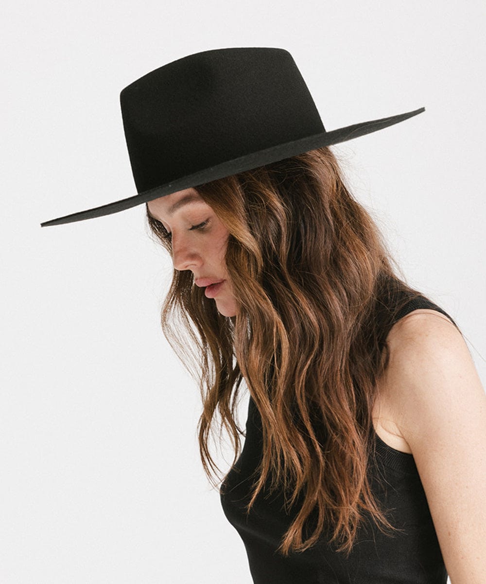 Woman wearing a black fedora hat and a black top, looking down against a plain background #color_black