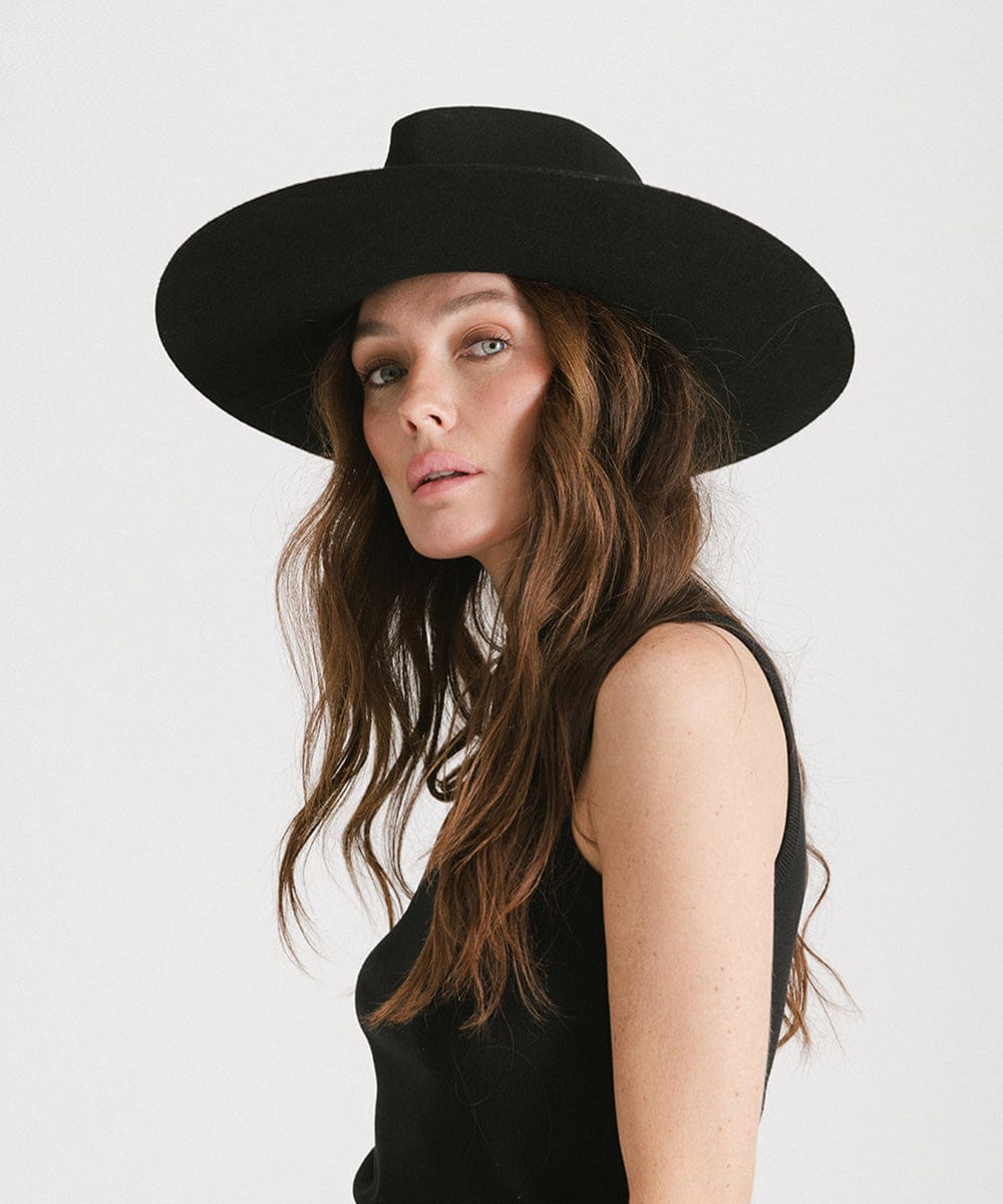 Woman wearing a black fedora hat and a black top, posing against a plain background #color_black