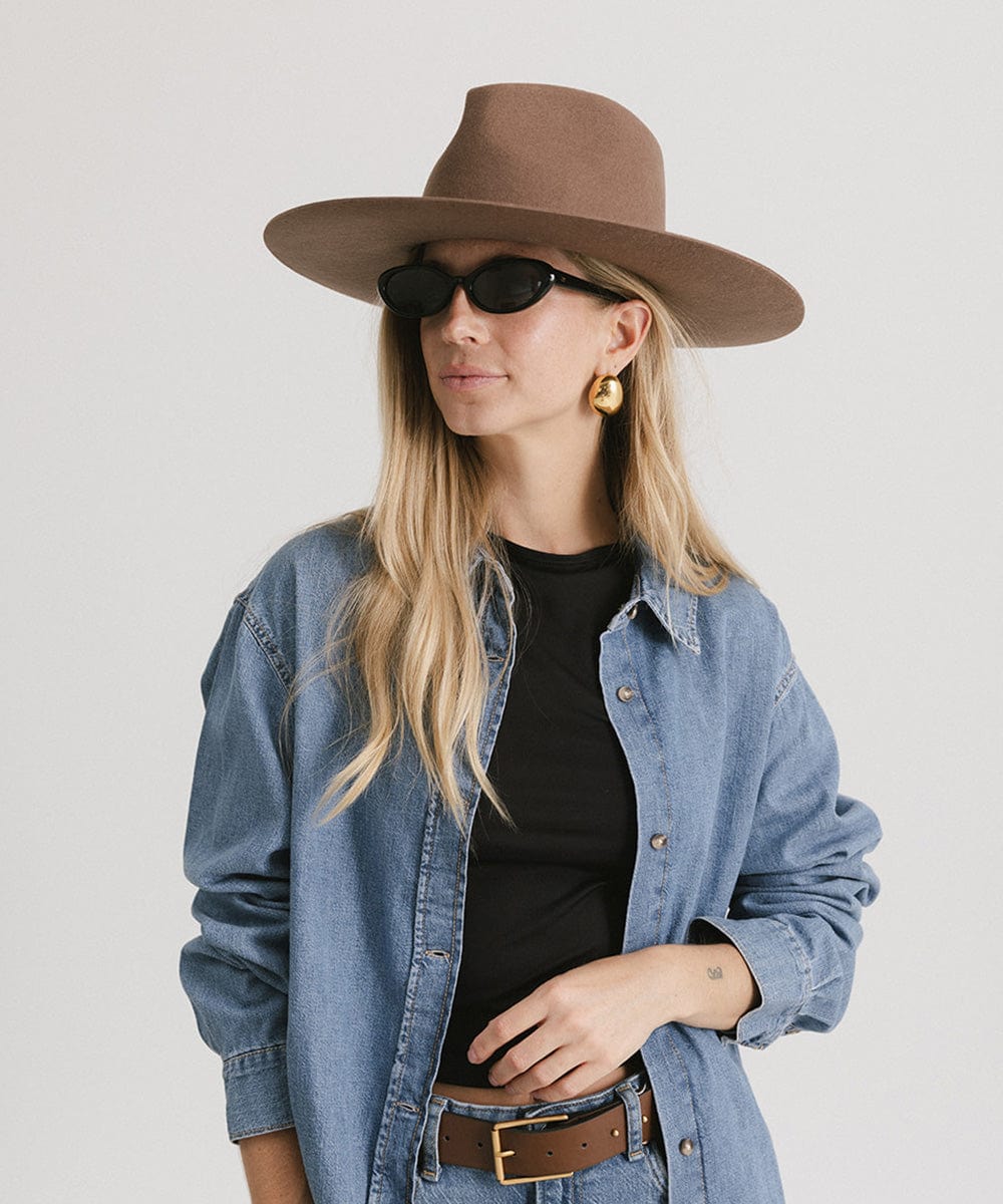 Woman wearing a chocolate colored fedora hat, sunglasses and a black t-shirt with a denim shirt, posing against a plain background #color_chocolate