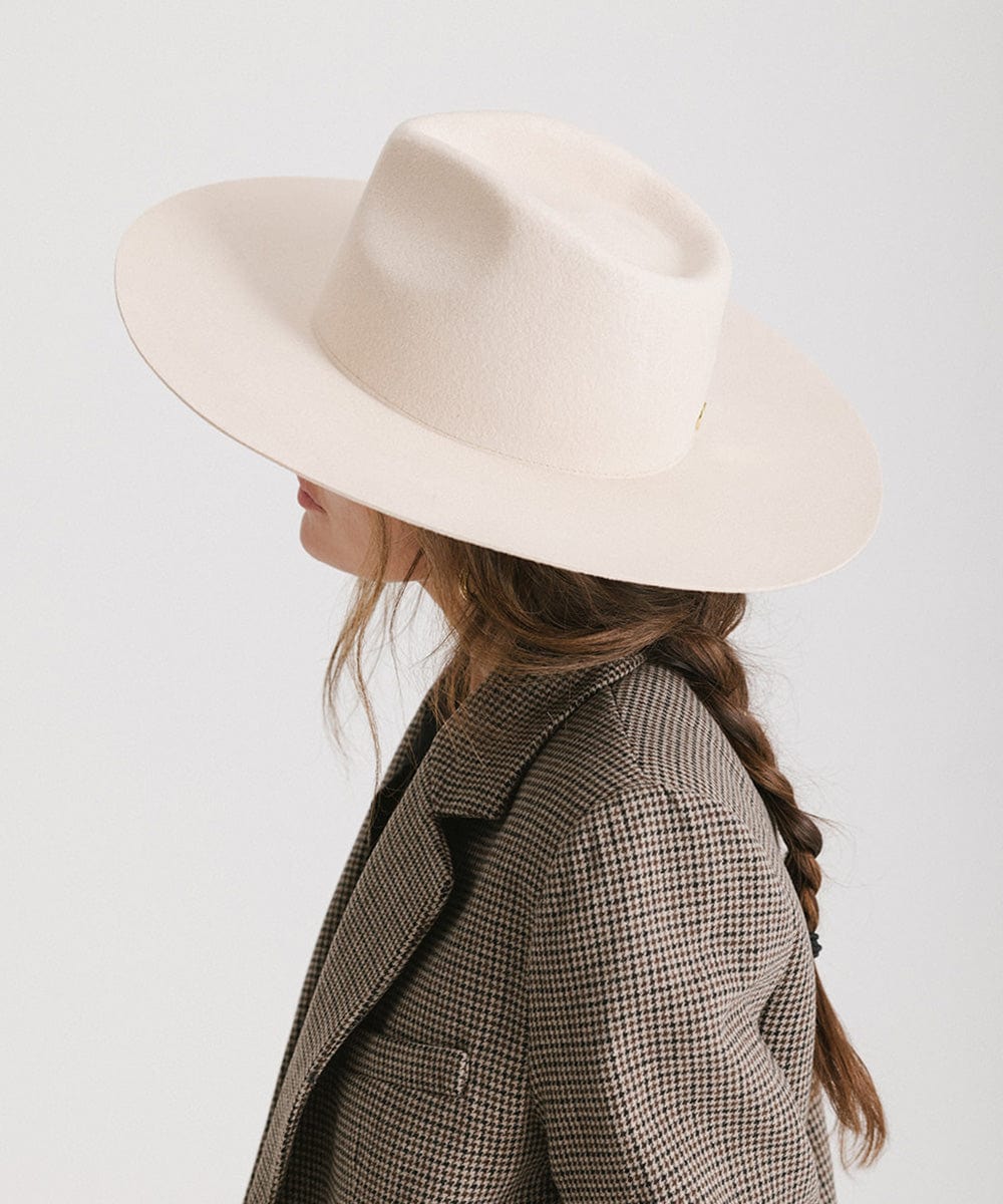 Person wearing a cream fedora hat and a blazer, facing sideways against a plain background #color_cream