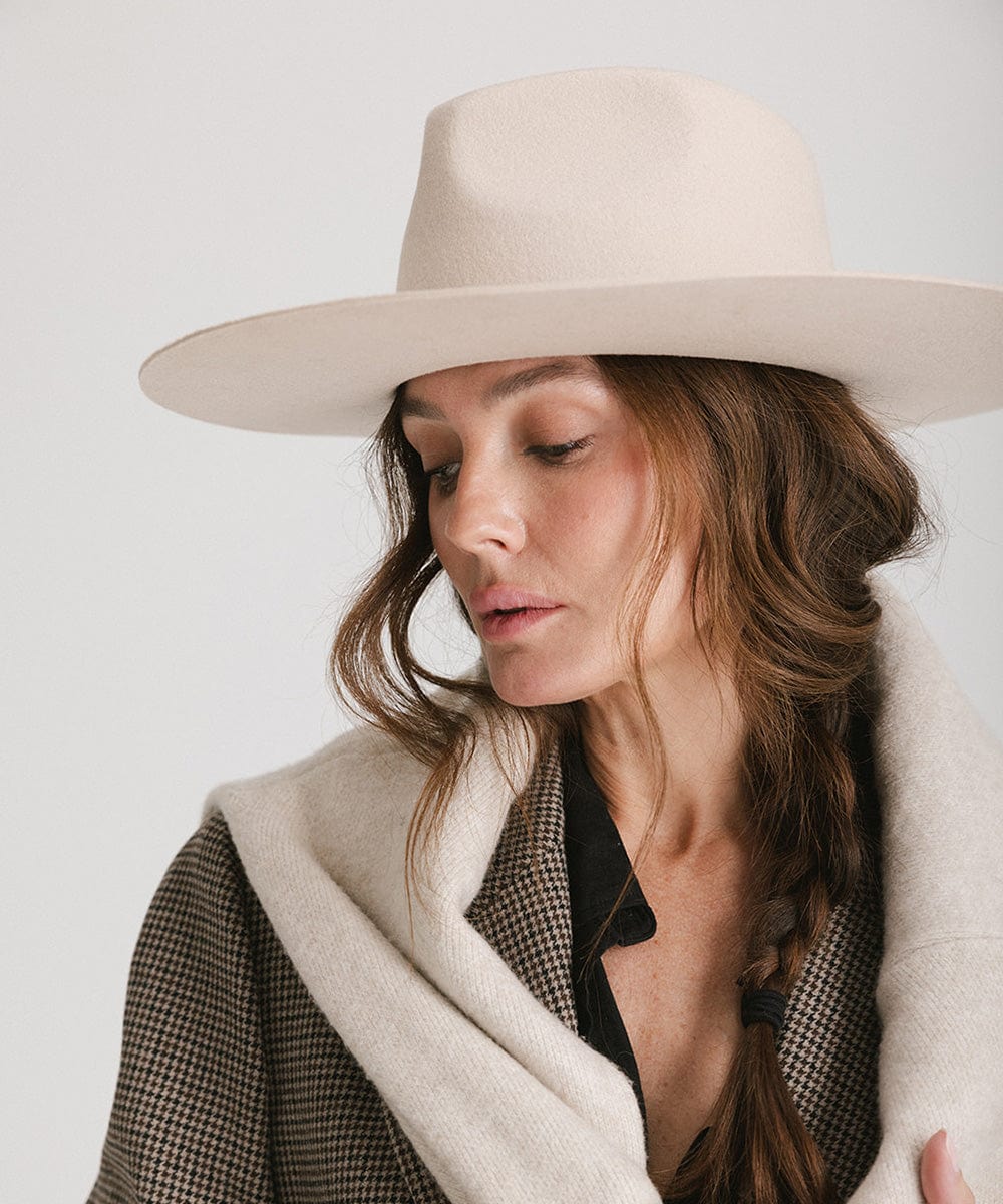 Woman with brown hair wearing a cream fedora hat and a blazer, looking sideways against a plain background #color_cream