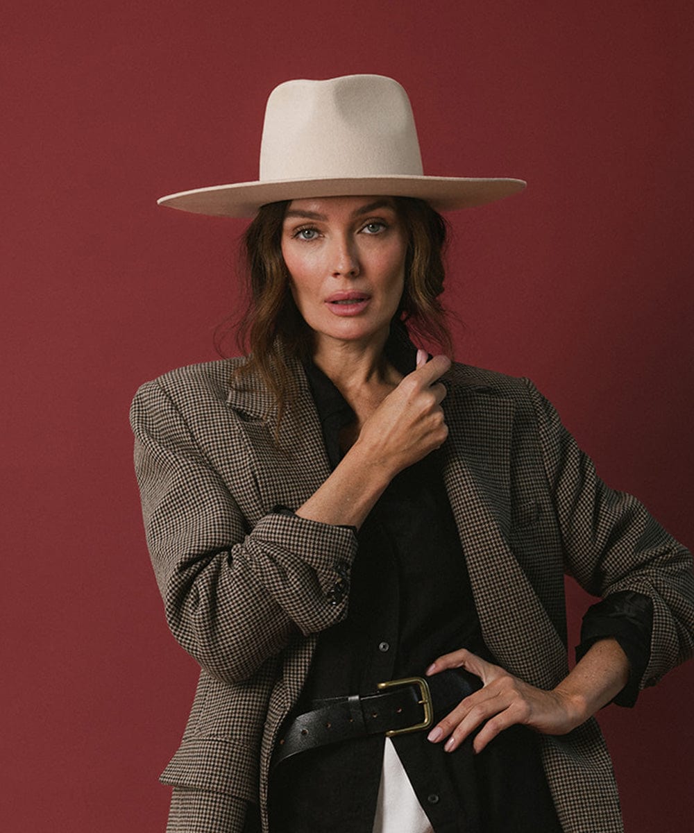 Woman wearing a cream fedora hat and a black shirt with a blazer against a red background #color_cream