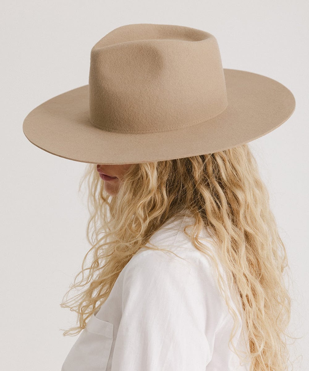 Woman wearing a tan fedora hat and a white shirt, facing sideways against a plain background  #color_tan