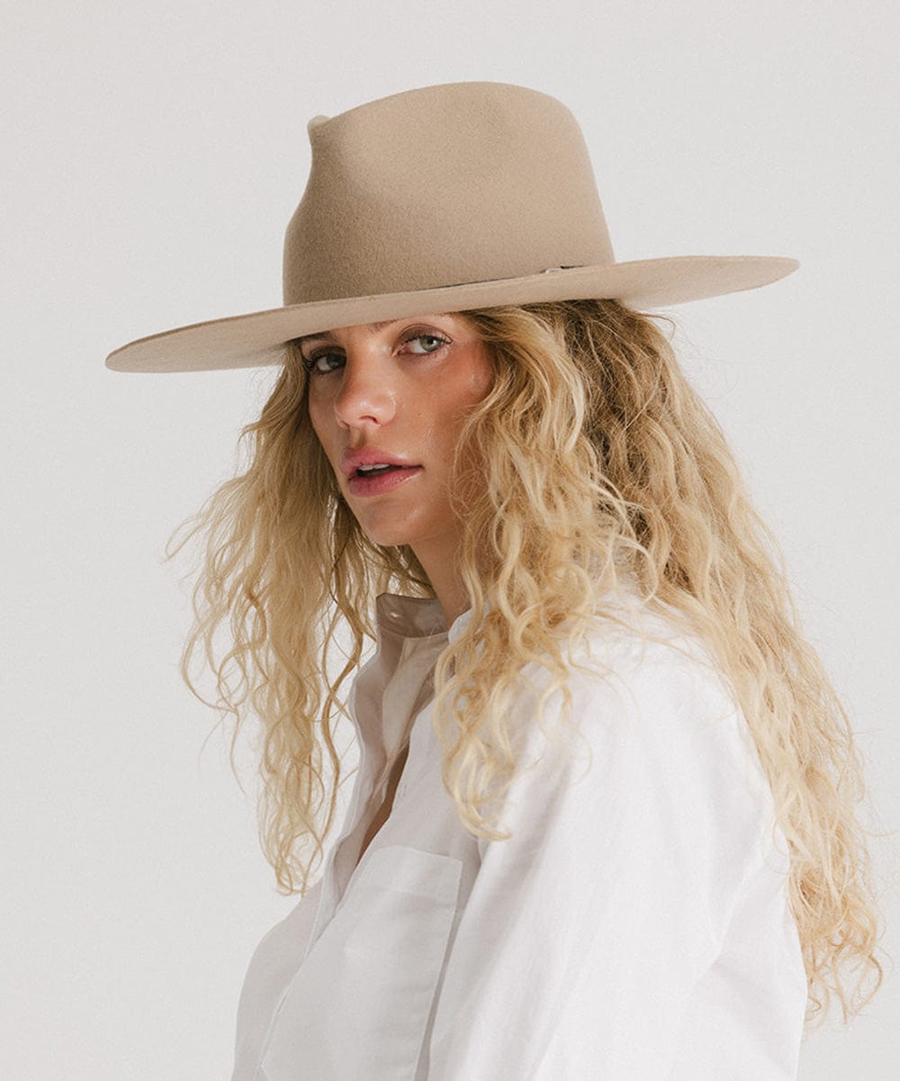 Woman wearing a tan fedora hat and a white shirt, posing against a plain background  #color_tan