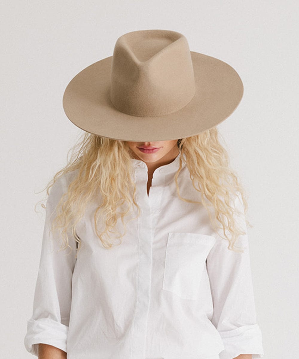 Woman wearing a tan fedora hat and a white shirt, looking down against a plain background  #color_tan