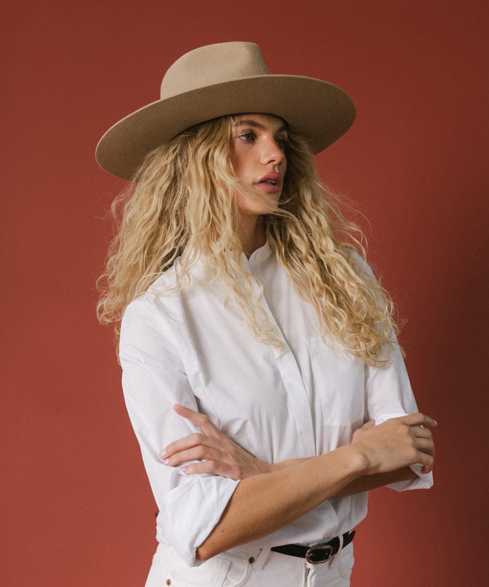 Woman wearing a tan fedora hat and a white shirt, looking sideways against a red background  #color_tan