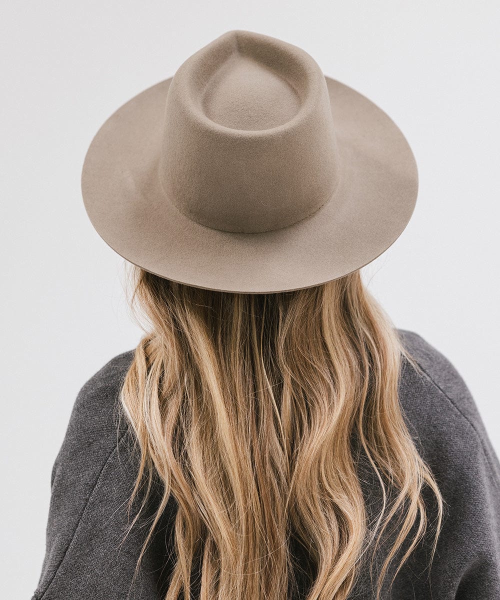 Woman wearing a sage fedora hat and a dark grey jacket, facing behind against a white background #color_sage