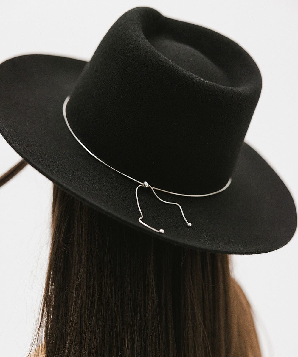 Woman wearing a black fedora hat with a band against a white background #color_black
