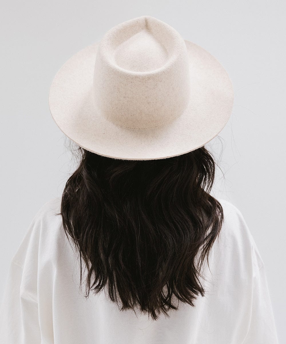 Woman wearing a mix ivory colored fedora hat and a white shirt, facing behind against a white background #color_mix ivory