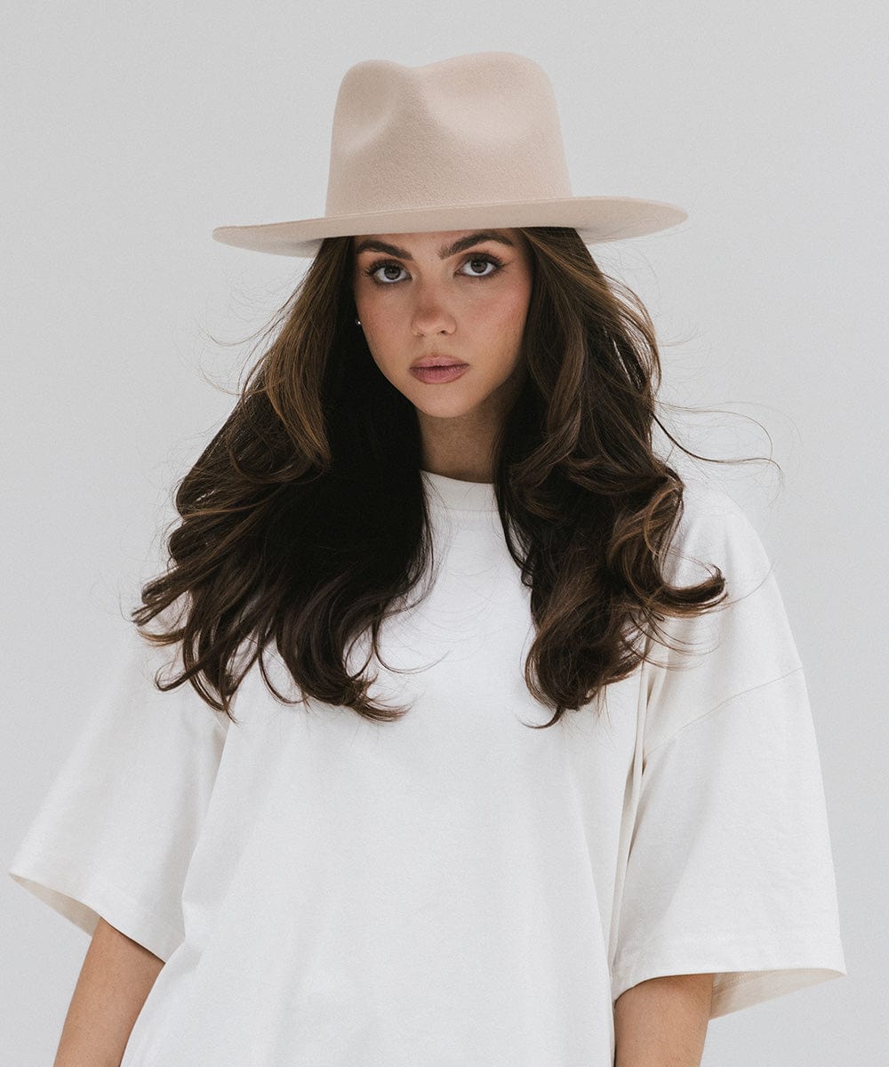 Woman wearing a cream fedora hat and a white shirt against a white background #color_cream