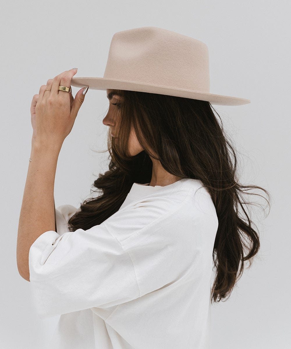 Woman wearing a cream fedora hat and a white shirt, facing sideways against a white background #color_cream