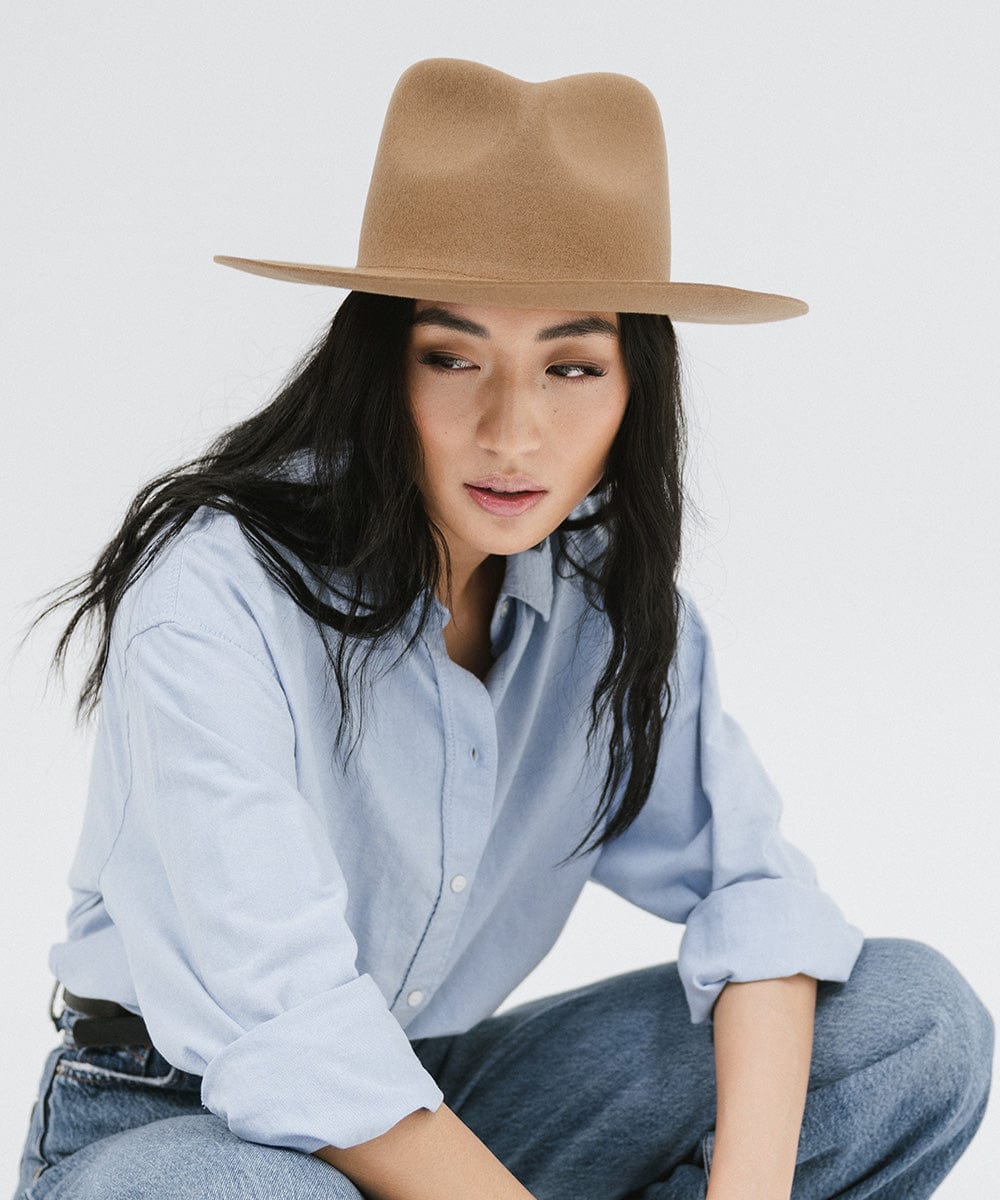 Woman wearing a brown fedora hat, a light blue shirt and blue jeans against a white background #color_brown