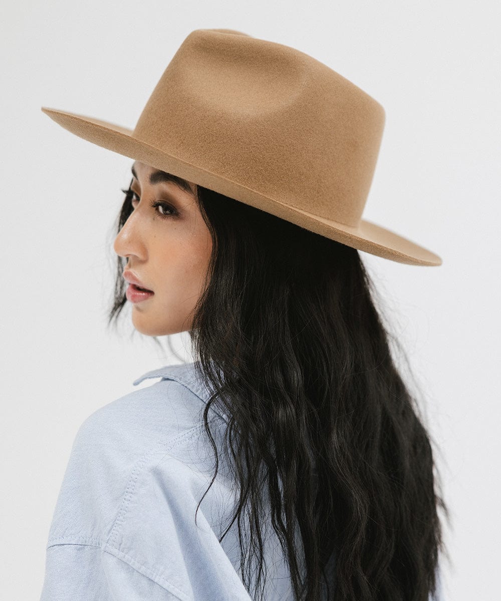 Woman wearing a brown fedora hat and a light blue shirt, looking sideways against a white background #color_brown
