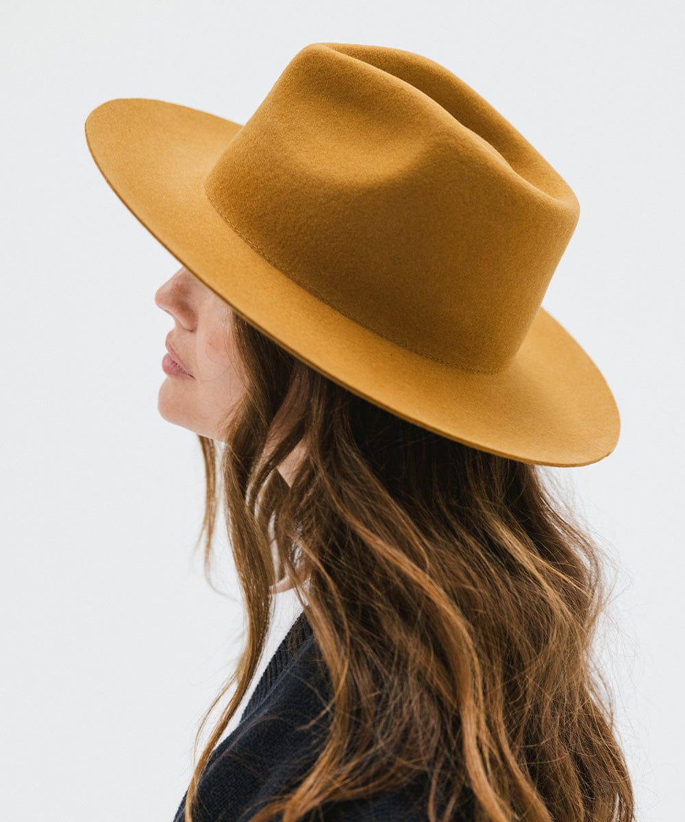 Woman wearing a cinnamon colored fedora hat and a dark blue shirt, facing sideways against a white background #color_cinnamon