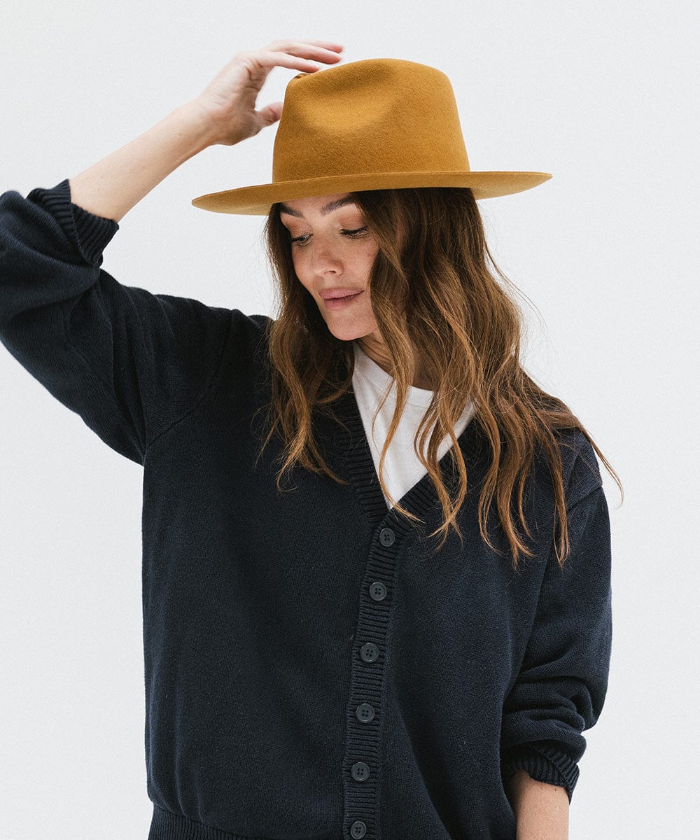 Woman wearing a cinnamon colored fedora hat and a dark blue shirt, looking down against a white background #color_cinnamon