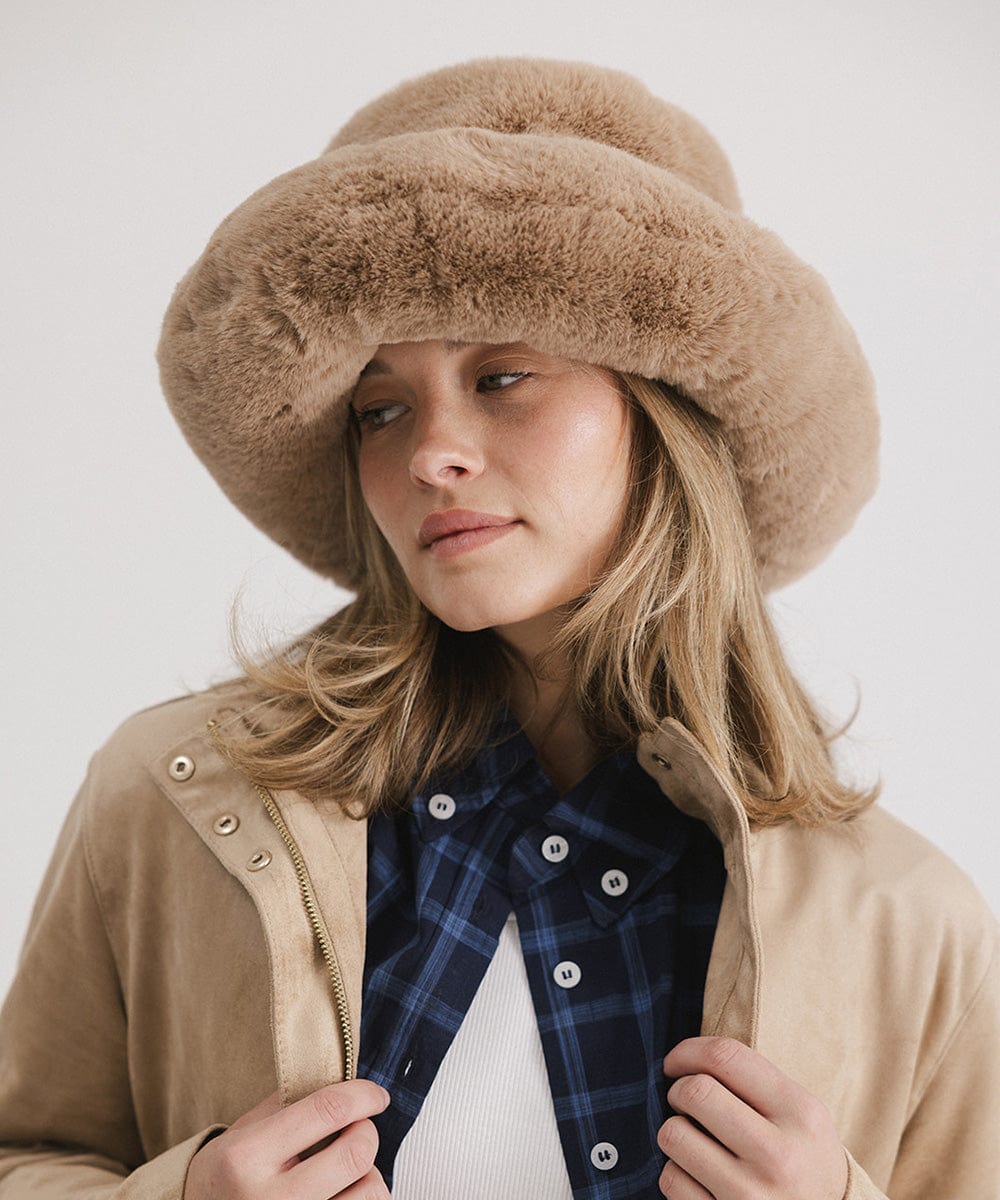 Woman wearing a tan faux fur bucket hat and a tan jacket against a plain background #color_tan