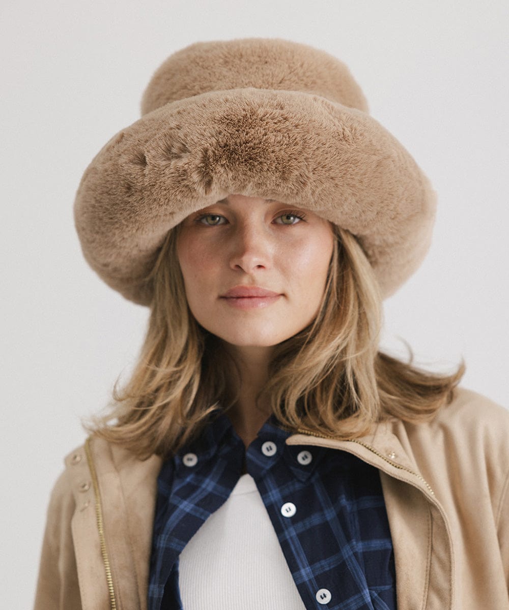 Woman wearing a tan faux fur bucket hat and a tan jacket against a plain background #color_tan