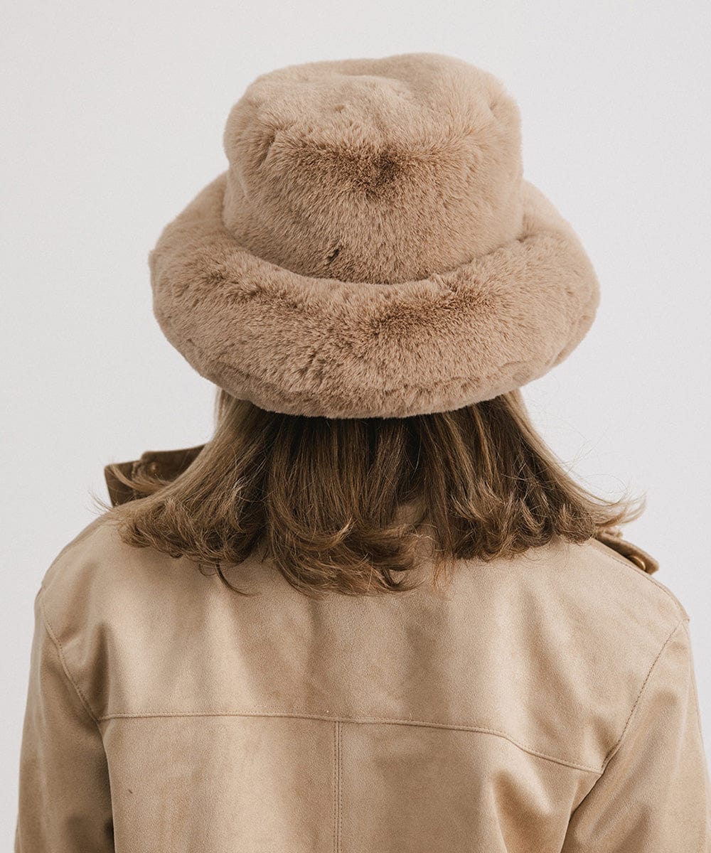 Person wearing a tan faux fur bucket hat and a tan jacket against a plain background #color_tan