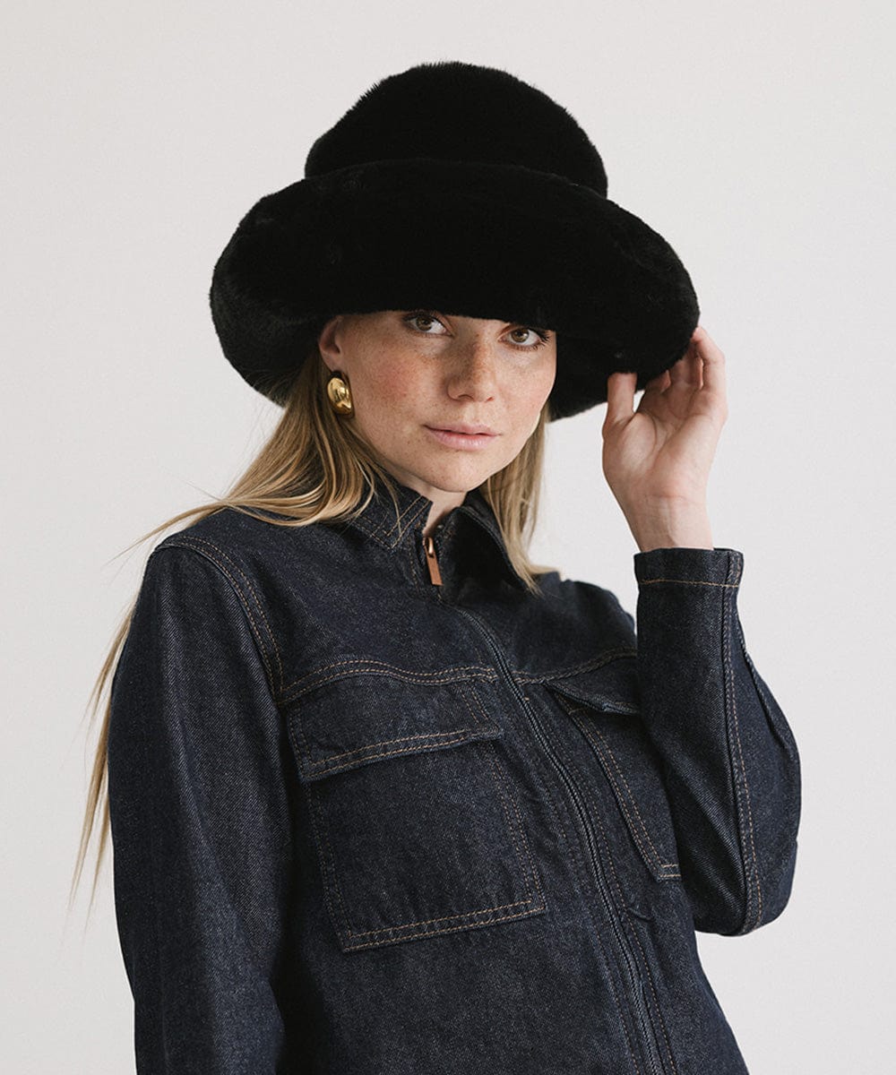 Woman wearing a black faux fur bucket hat and a dark blue denim jacket against a plain background #color_black