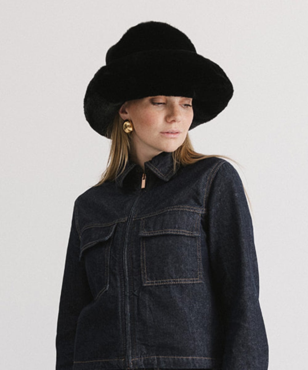 Woman wearing a black faux fur bucket hat and a dark blue denim jacket against a plain background #color_black
