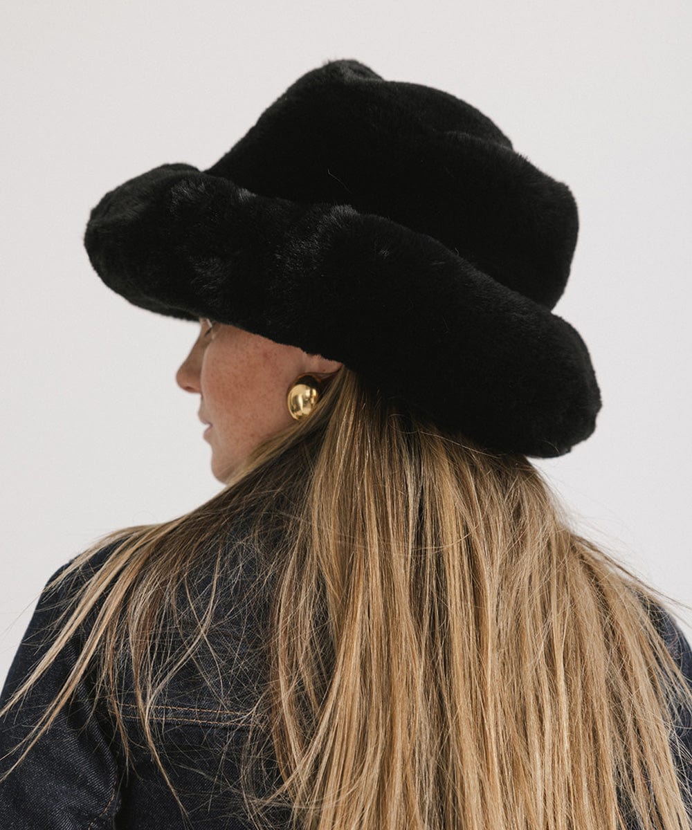 Person with long hair wearing a black faux fur bucket hat against a plain background #color_black