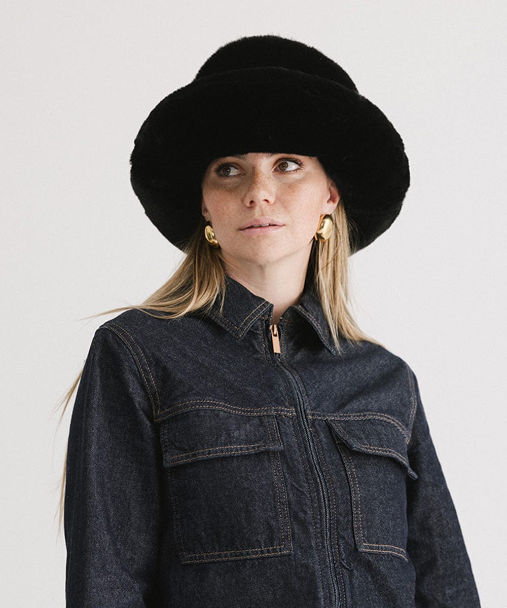 Woman wearing a black faux fur bucket hat and a dark blue denim jacket against a plain background #color_black