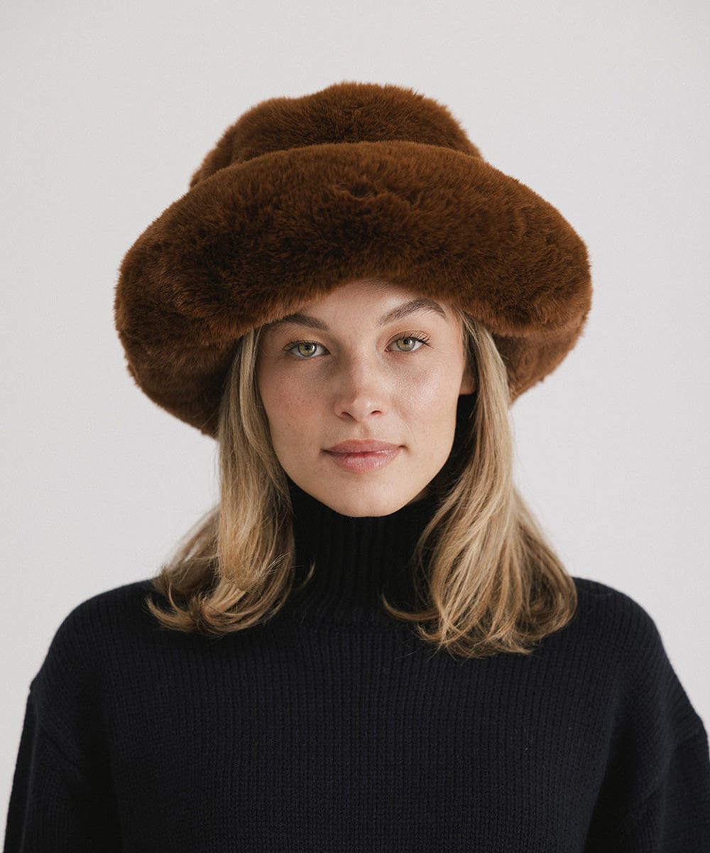 Woman wearing a brown faux fur bucket hat and a dark blue sweater against a plain background #color_brown