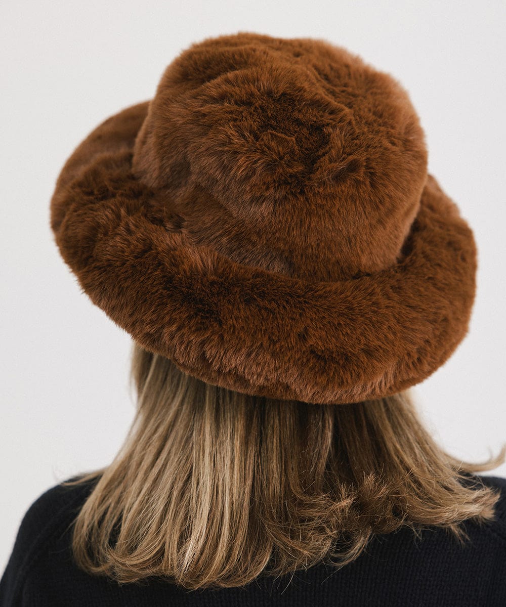 Person wearing a brown faux fur bucket hat against a plain background #color_brown