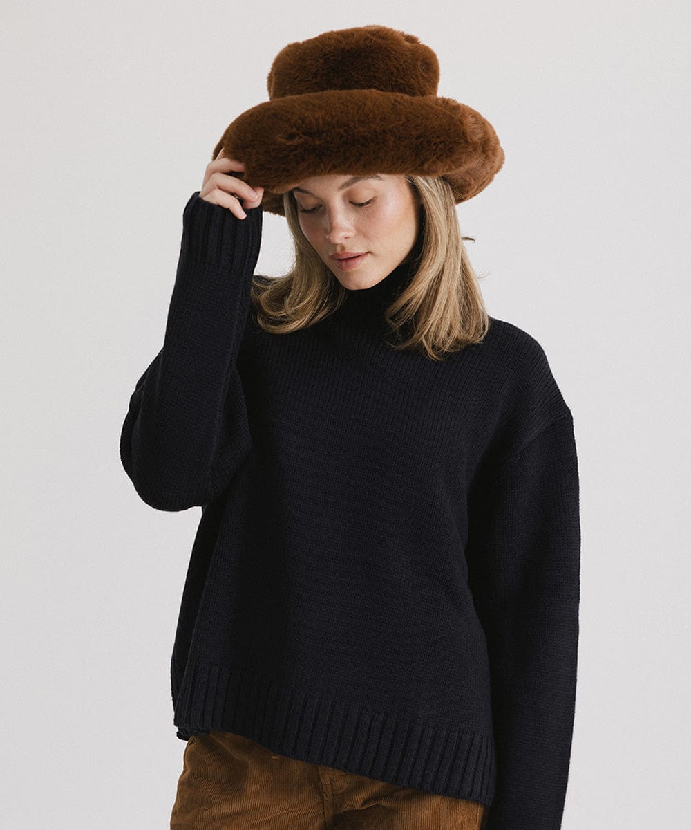 Woman wearing a brown faux fur bucket hat and a dark blue sweater against a plain background #color_brown