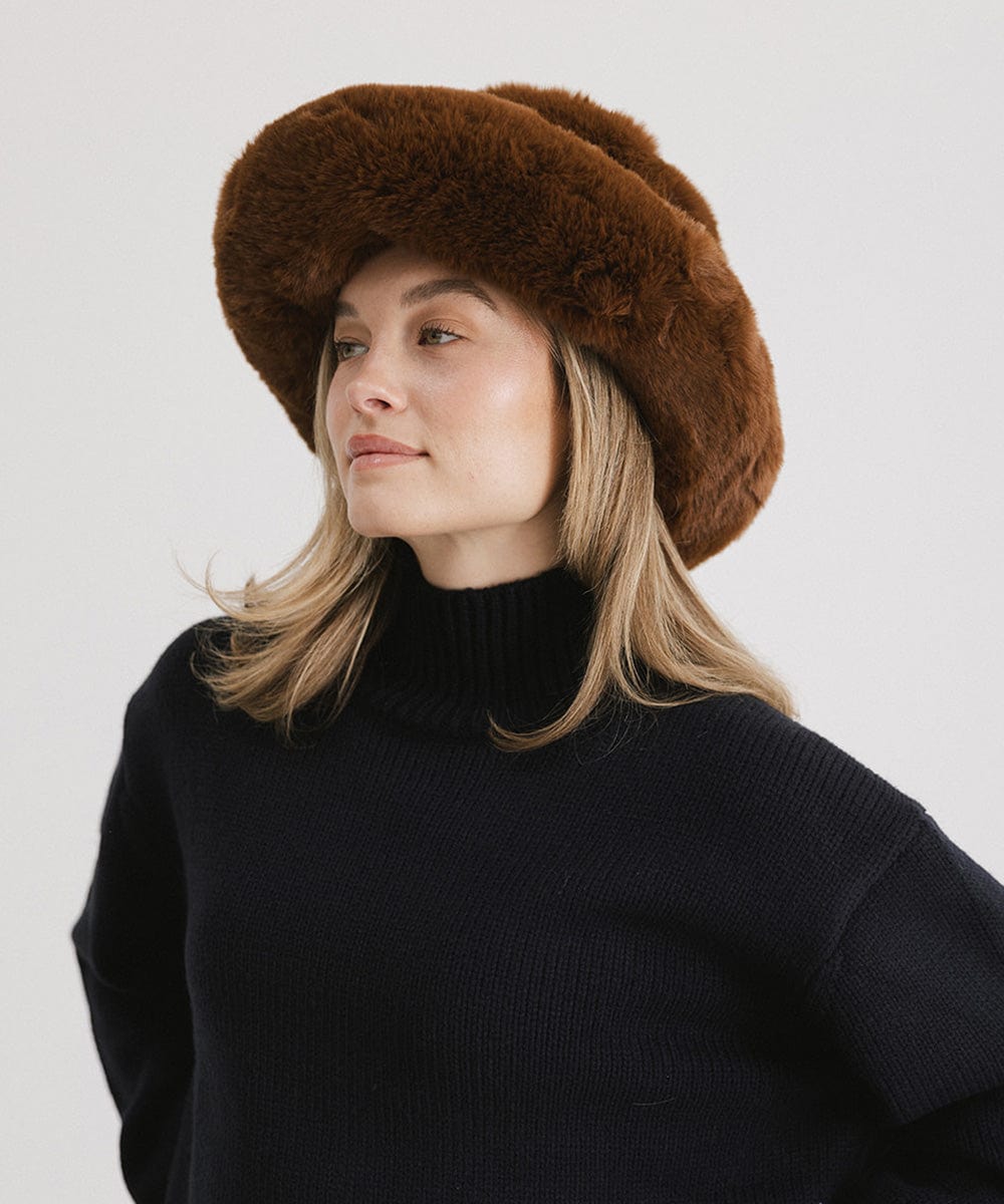 Woman wearing a brown faux fur bucket hat and a dark blue sweater against a plain background #color_brown