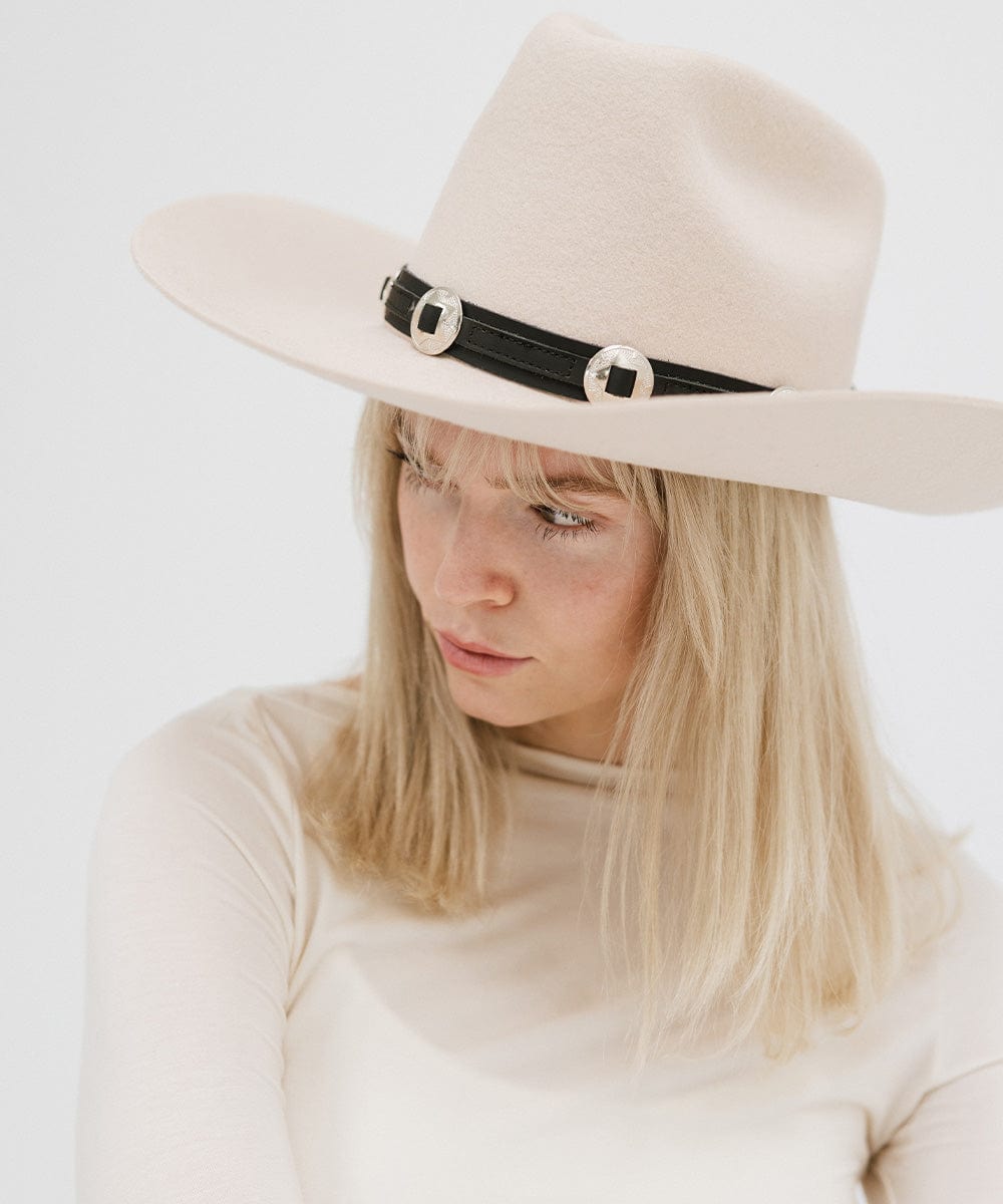 A woman wearing a white hat with a black western style genuine leather hat band and a white top against a plain background #color_black