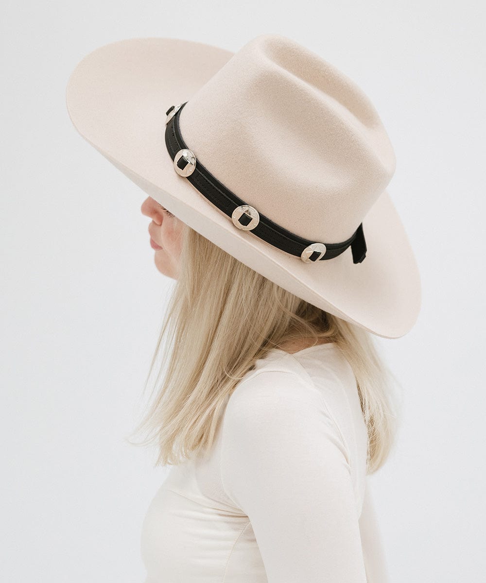 A woman wearing a white hat with a black western style genuine leather hat band and a white top, facing sideways against a plain background #color_black