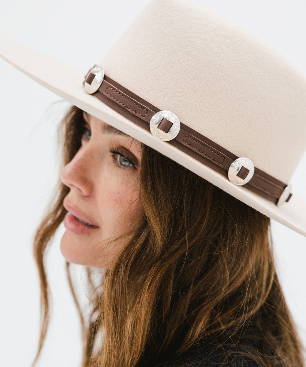 Woman wearing a white hat with a chocolate colored western style  genuine leather hat band, facing sideways against a plain background #color_chocolate