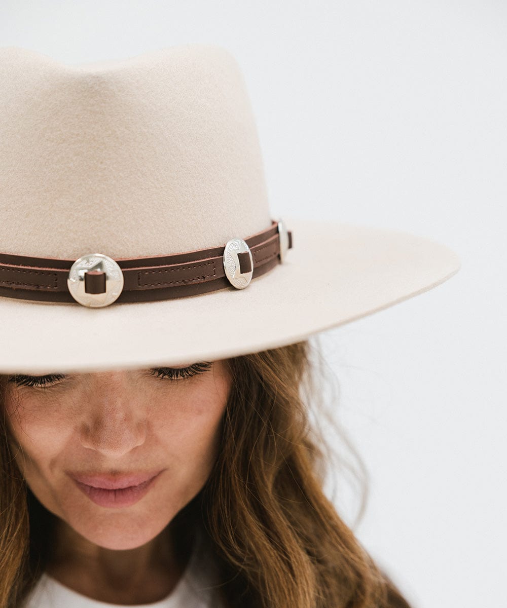 Close up image of a woman wearing a white hat with a chocolate colored western style  genuine leather hat band against a plain background #color_chocolate