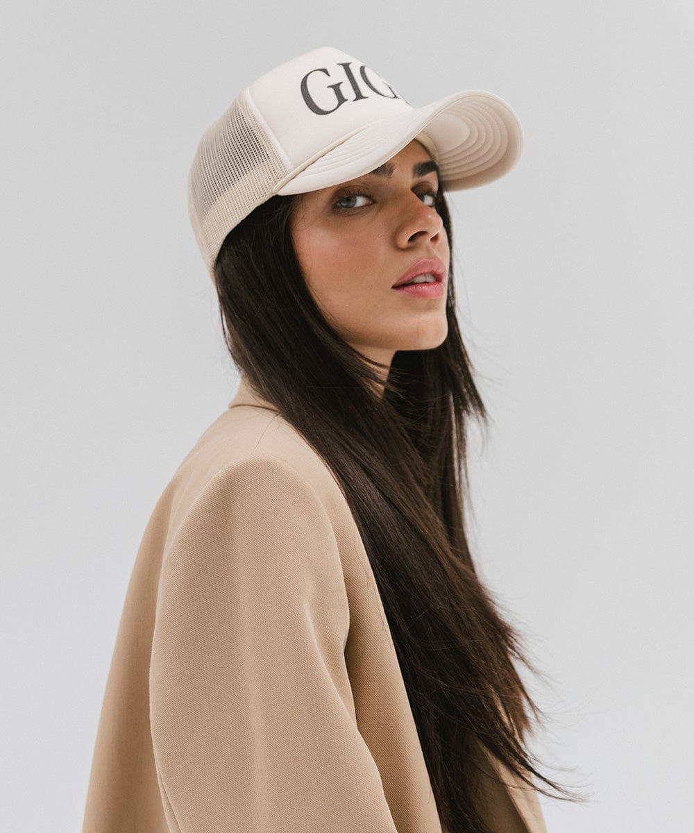 Woman wearing a cream cap with 'GIGI' text and a beige coat, posing sideways against a plain background  #color_cream