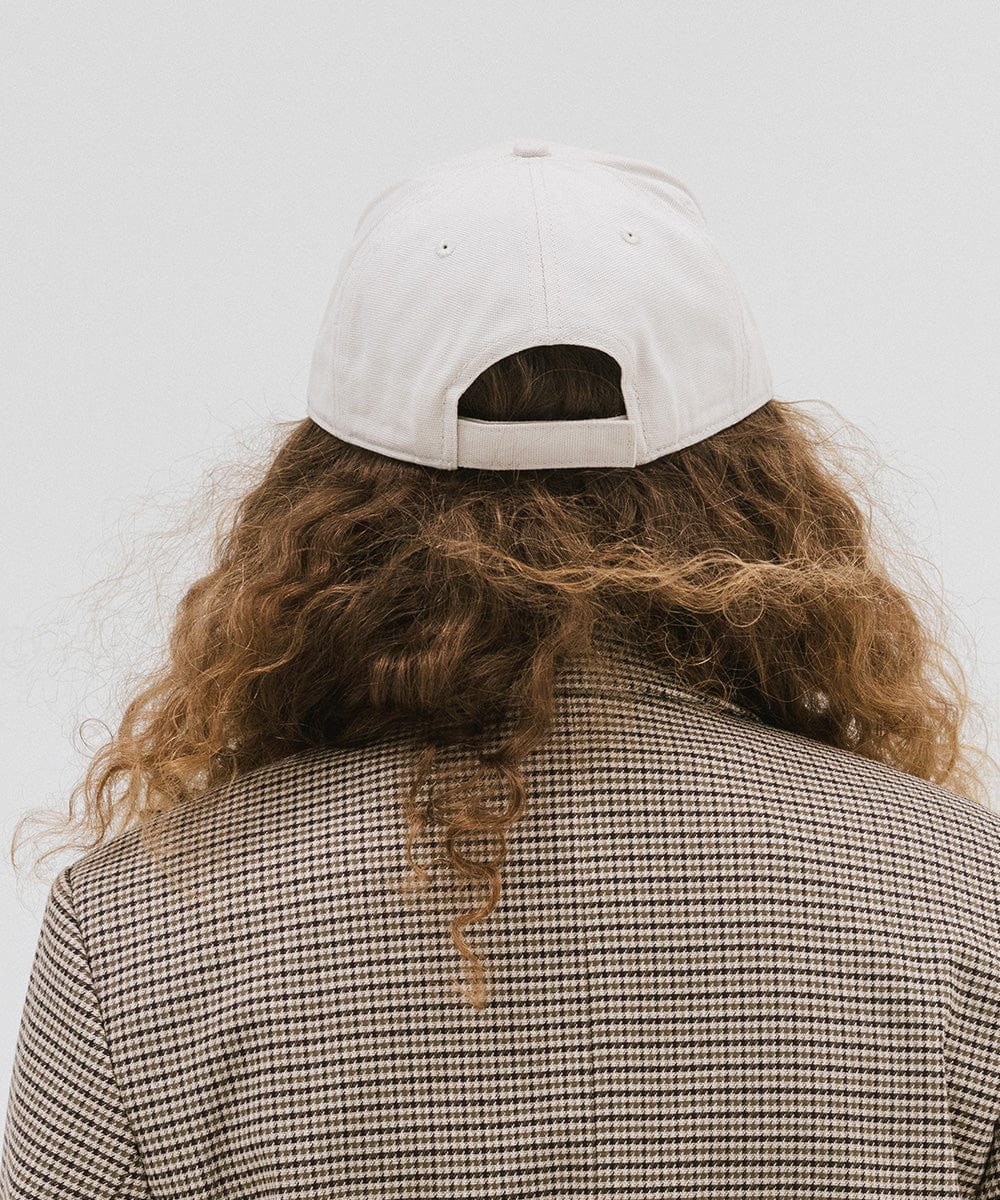 Woman wearing a cream trucker hat a coat  against a plain background #color_cream