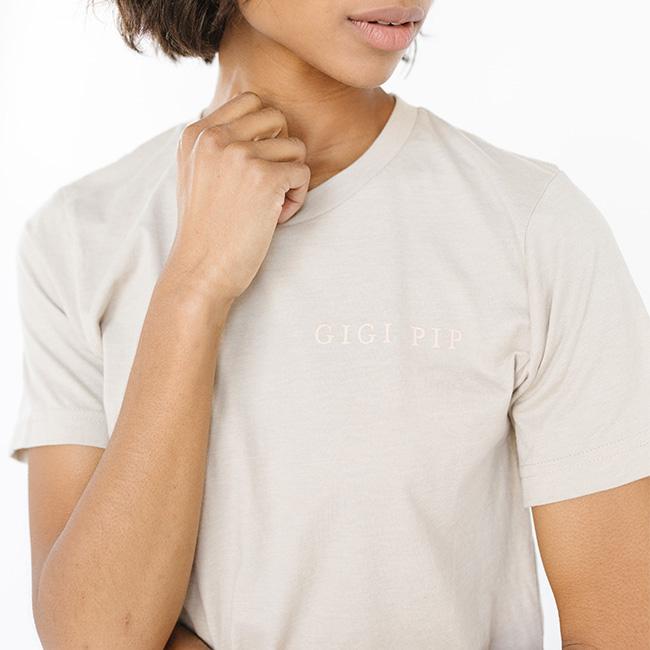 Woman wearing a sand colored t-shirt with 'GIGI PIP' text against a white background #color_sand