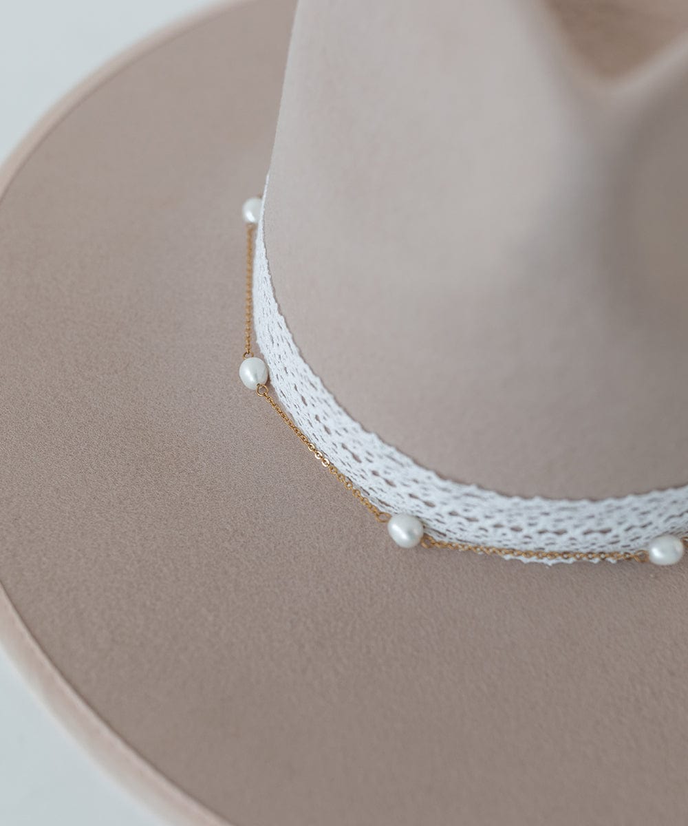 Close up image of a beige hat with a white band and a  gold pearl chain band on a plain background #color_gold